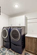 Laundry area with cabinet space, a textured ceiling, and washer and clothes dryer