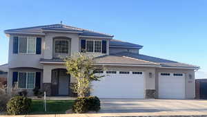 Traditional-style home featuring a garage, driveway, stucco siding, and a tiled roof