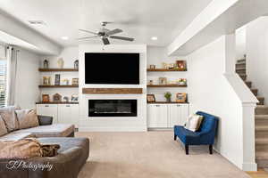 Living room featuring a large fireplace, light carpet, a ceiling fan, stairway, and recessed lighting