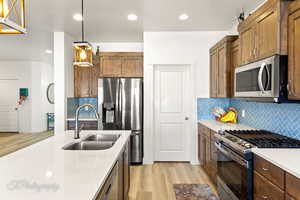 Kitchen featuring stainless steel appliances, light wood-type flooring, recessed lighting, hanging light fixtures, and light stone counters