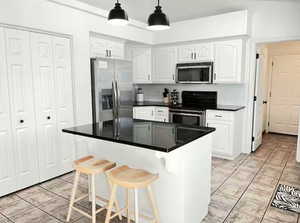 Kitchen with white cabinetry, stainless steel appliances, a breakfast bar area, and hanging light fixtures