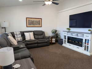 Living room featuring carpet, lofted ceiling, a glass covered fireplace, and a ceiling fan