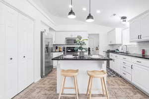 Kitchen featuring pendant lighting, white cabinetry, appliances with stainless steel finishes, a breakfast bar, and decorative backsplash