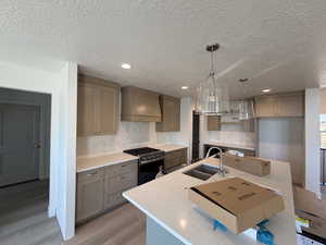 Kitchen featuring tasteful backsplash, pendant lighting, stainless steel range with gas stovetop, premium range hood, and a textured ceiling