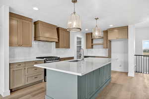 Kitchen featuring gas range, decorative backsplash, custom range hood, light stone countertops, and recessed lighting