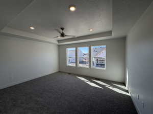 Empty room with a raised ceiling, carpet flooring, a textured ceiling, recessed lighting, and ceiling fan