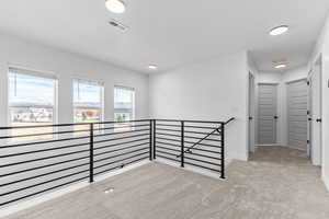 Corridor with light colored carpet and an upstairs landing