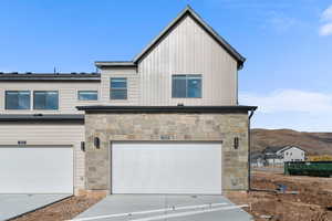 View of front of property with concrete driveway, stone siding, board and batten siding, and a garage