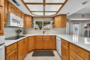 Kitchen featuring brown cabinetry, open shelves, backsplash, white appliances, and plenty of natural light