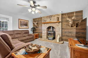 Carpeted living area with a wood stove, a textured ceiling, ceiling fan, and wooden walls
