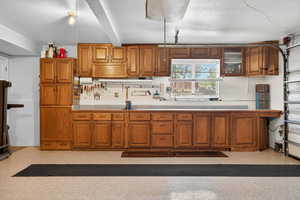 Kitchen with brown cabinets, tile counters, backsplash, beamed ceiling, and glass insert cabinets