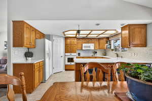 Kitchen featuring backsplash, brown cabinets, white appliances, a peninsula, and light tile patterned floors