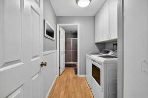 Laundry area featuring light wood-style floors, a textured ceiling, independent washer and dryer, and cabinet space