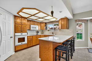 Kitchen featuring backsplash, brown cabinetry, a breakfast bar, white appliances, and a peninsula