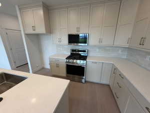 Kitchen featuring appliances with stainless steel finishes, light wood-style flooring, tasteful backsplash, light stone counters, and recessed lighting