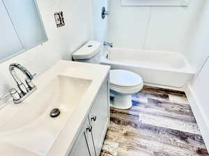 Bathroom with a textured wall, light wood-style floors, vanity, and shower / washtub combination