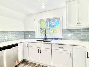 Kitchen featuring white cabinetry, stainless steel dishwasher, a textured ceiling, light wood-style floors, and backsplash