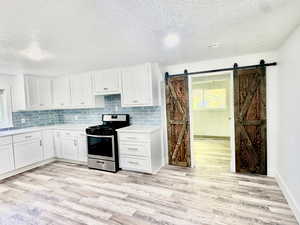 Kitchen featuring stainless steel range with gas cooktop, tasteful backsplash, white cabinetry, a textured ceiling, and light wood-style flooring