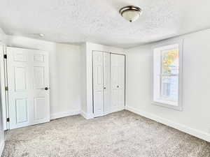 Unfurnished bedroom featuring a textured ceiling, a closet, and light colored carpet