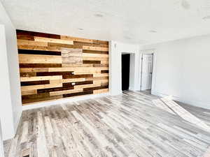 Unfurnished room featuring wood walls, light wood-type flooring, and a textured ceiling