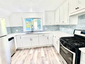 Kitchen with stainless steel appliances, white cabinetry, a textured ceiling, light wood-style flooring, and decorative backsplash
