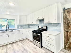 Kitchen with a barn door, stainless steel range with gas stovetop, white cabinets, a textured ceiling, and decorative backsplash