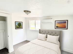 Bedroom featuring a wall mounted AC, light colored carpet, and a textured ceiling