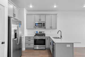 Kitchen with stainless steel appliances, a peninsula, gray cabinetry, light wood-style floors, and light stone countertops