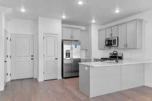 Kitchen with stainless steel appliances, light wood-type flooring, a peninsula, recessed lighting, and light stone countertops