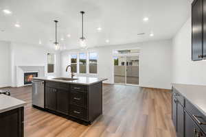 Kitchen featuring open floor plan, a glass covered fireplace, hanging light fixtures, light wood-style flooring, and stainless steel dishwasher