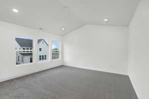 Empty room featuring vaulted ceiling, dark colored carpet, and recessed lighting