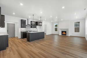 Kitchen featuring open floor plan, a kitchen island with sink, decorative light fixtures, a lit fireplace, and tasteful backsplash