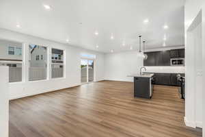 Kitchen featuring open floor plan, an island with sink, hanging light fixtures, light wood-style flooring, and recessed lighting