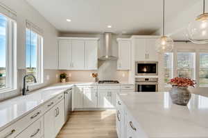 Kitchen with white cabinetry, pendant lighting, tasteful backsplash, wall chimney range hood, and recessed lighting