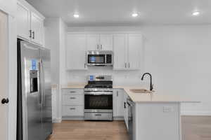 Kitchen with a peninsula, appliances with stainless steel finishes, white cabinetry, light wood-type flooring, and recessed lighting