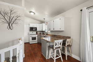 Kitchen with a peninsula, gas range gas stove, a breakfast bar area, white cabinets, and vaulted ceiling
