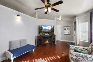Living room with dark wood-style flooring, a ceiling fan, and a glass covered fireplace