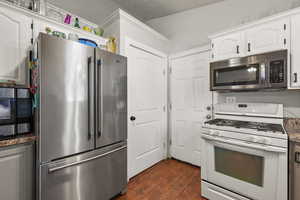 Kitchen featuring appliances with stainless steel finishes, dark wood finished floors, white cabinets, and dark stone countertops