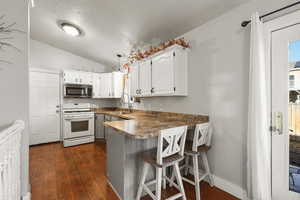 Kitchen featuring white cabinetry, a kitchen breakfast bar, white range with gas cooktop, lofted ceiling, and dark wood-style floors
