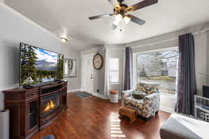 Living room featuring a textured ceiling, wood-type flooring, a ceiling fan, and a glass covered fireplace