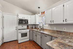 Kitchen with dark countertops, stainless steel appliances, vaulted ceiling, decorative light fixtures, and dark wood-type flooring