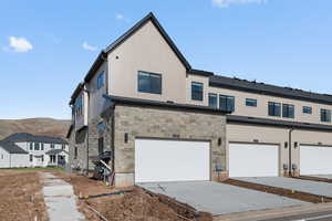 Back of property with stone siding, driveway, an attached garage, and a mountain view