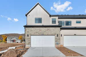 View of front facade with concrete driveway, stone siding, a garage, and board and batten siding