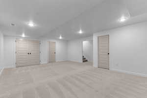 Finished below grade area featuring light carpet, a textured ceiling, and stairway