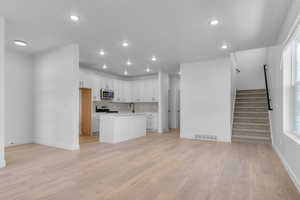 Kitchen with open floor plan, white cabinets, a center island with sink, light countertops, and light wood finished floors