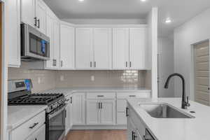 Kitchen featuring appliances with stainless steel finishes, white cabinets, decorative backsplash, light wood-style flooring, and light stone counters