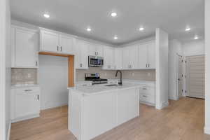 Kitchen with white cabinetry, backsplash, light wood-type flooring, stainless steel appliances, and recessed lighting