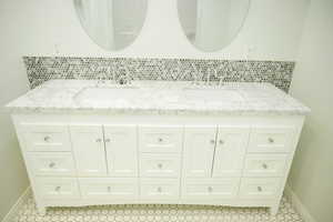Full bathroom with double vanity, tasteful backsplash, and light tile patterned floors