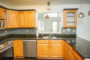 Kitchen with glass insert cabinets, decorative backsplash, stainless steel appliances, and dark granite counters