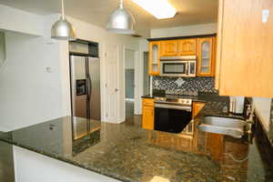 Kitchen with glass insert cabinets, stainless steel appliances, dark stone counters, backsplash, and pendant lighting